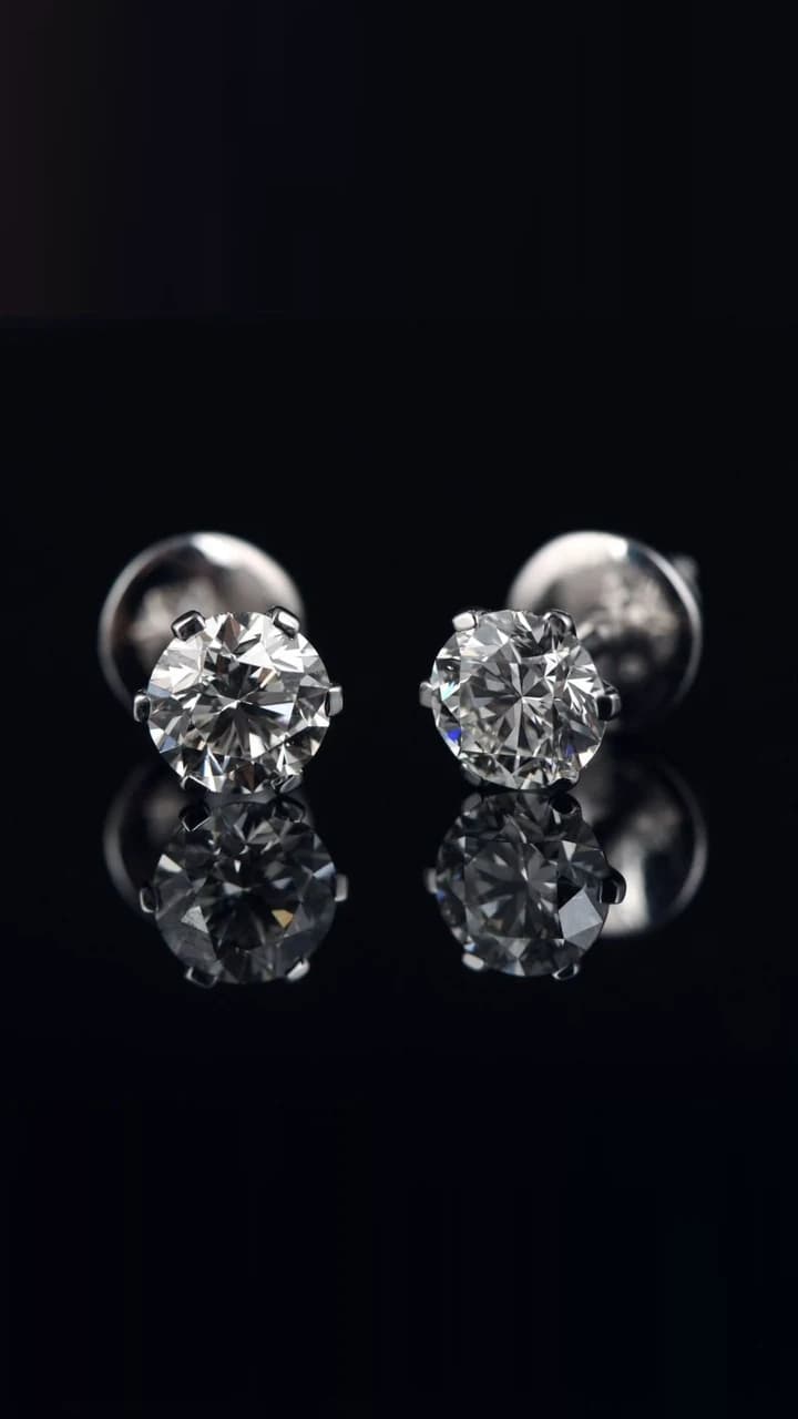 A pair of brilliant-cut diamond solitaire studs, photographed on black.