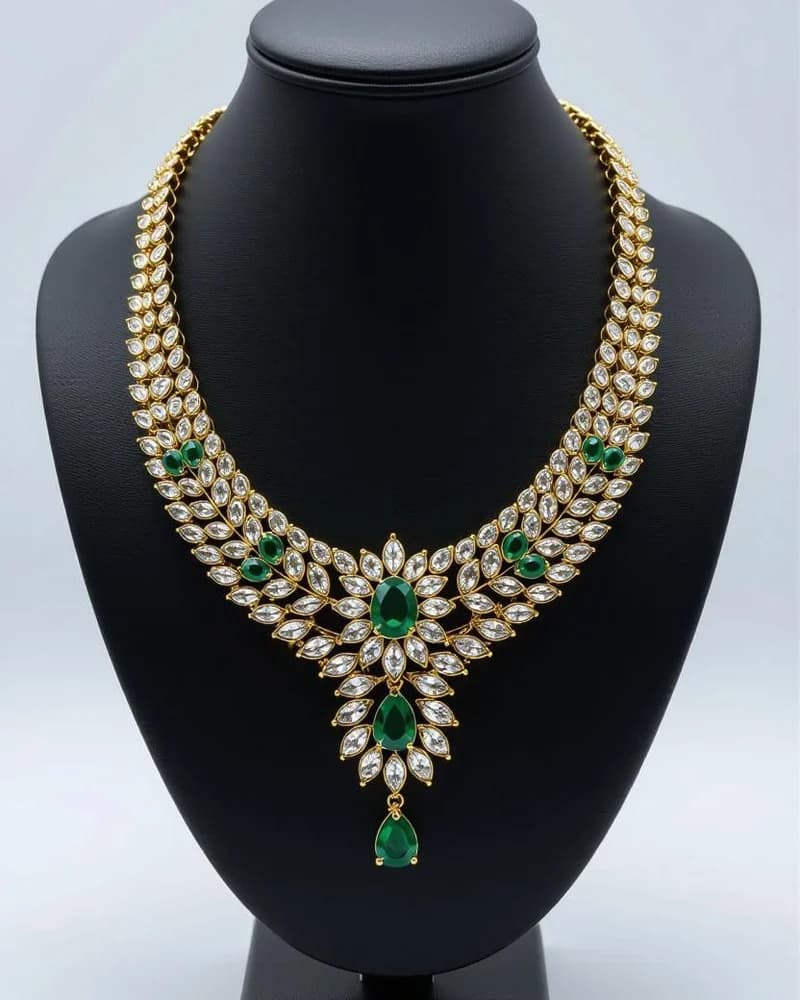 A wide yellow-gold and emerald bridal collar with a single emerald drop, on a black bust.