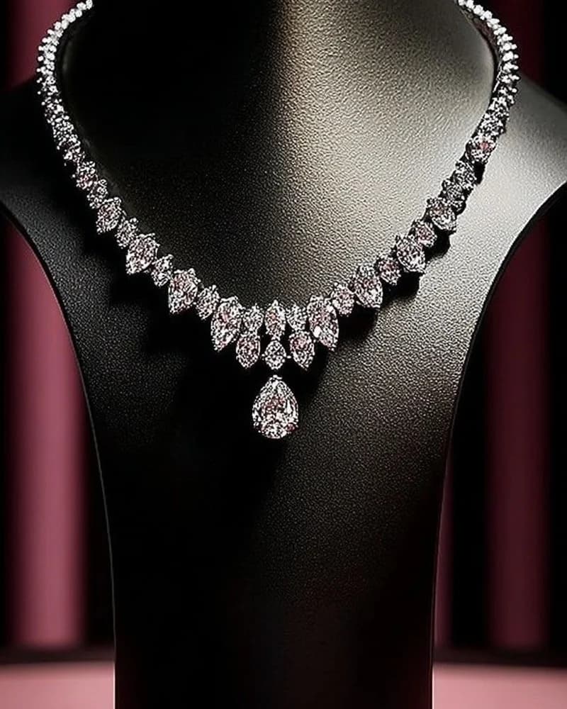 A graduated diamond rivière with a single pear-cut drop, on a black bust.