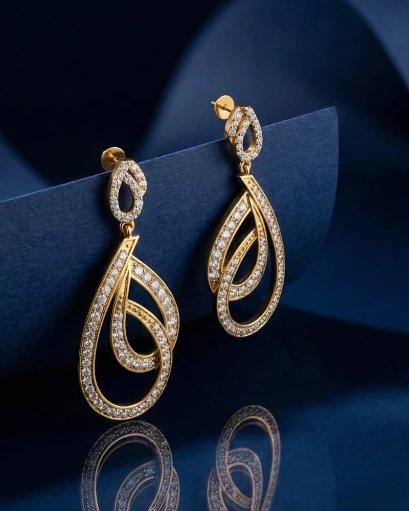 A pair of gold and diamond open teardrop loop earrings on blue.