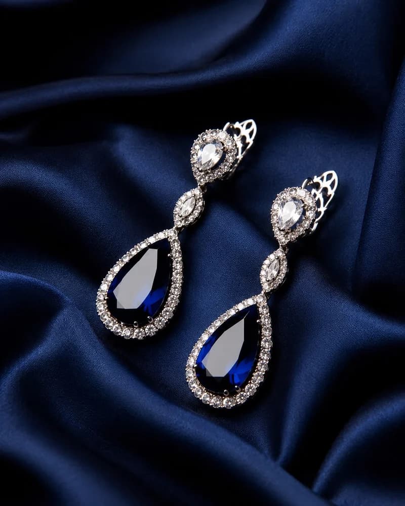 A pair of sapphire and diamond double-drop earrings on blue silk.