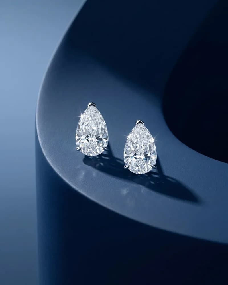 A pair of pear-cut diamond solitaire studs on blue.