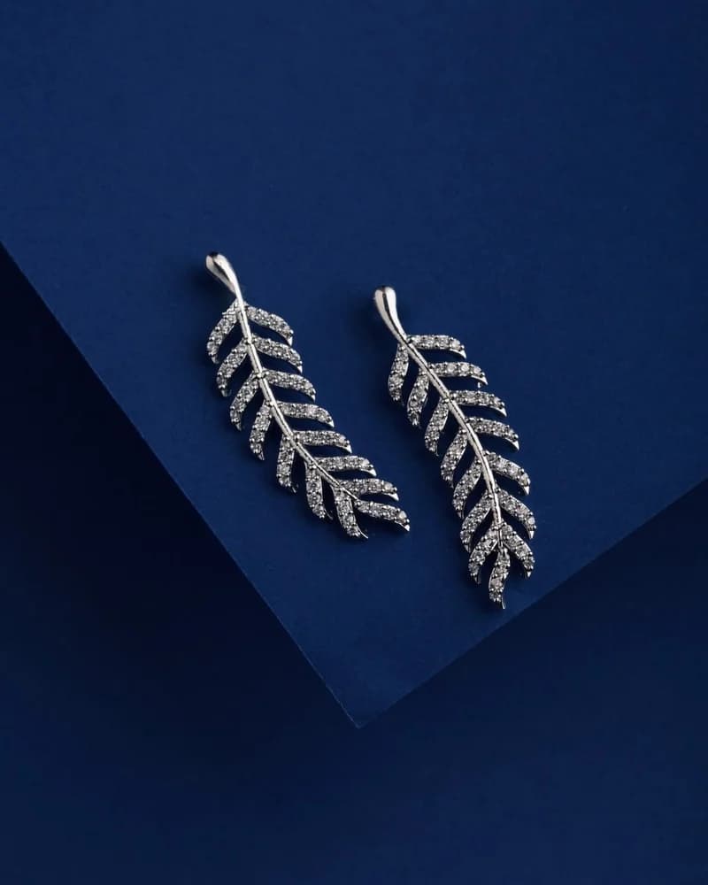 A pair of diamond feather ear climbers on blue.