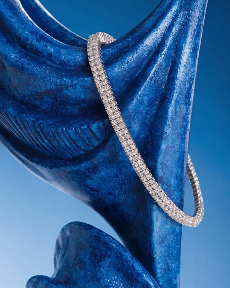 A fine diamond tennis bracelet draped over blue velvet.