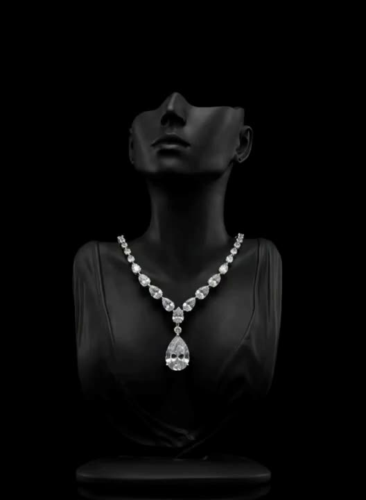 A diamond necklace with a pear-cut drop, on a dark mannequin bust.